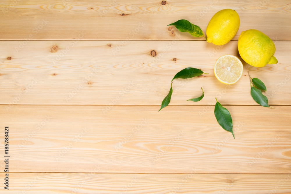 wooden light background with yellow lemons and green leaves