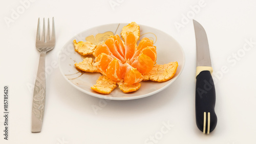 Раскрытый мандарин с кожурой на тарелке, нож и вилка.