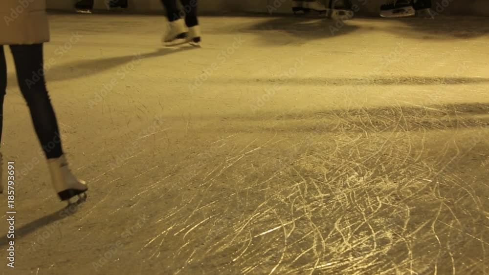 A lot of people skate on ice rink, only legs are visible. Men, women