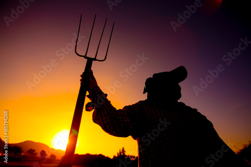 Silhouette, farmer holding pitchfork in sunset.