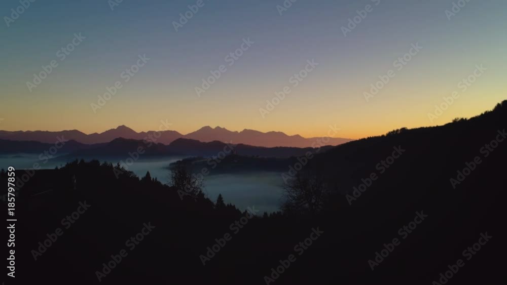 Aerial view of fog coverage the mountains forest at sunrise. Distant mountain range and thin layer of clouds on the valleys. Aerial view of fog coverage the mountains forest at sunrise. Distant mountain range and thin layer of clouds on the valleys.