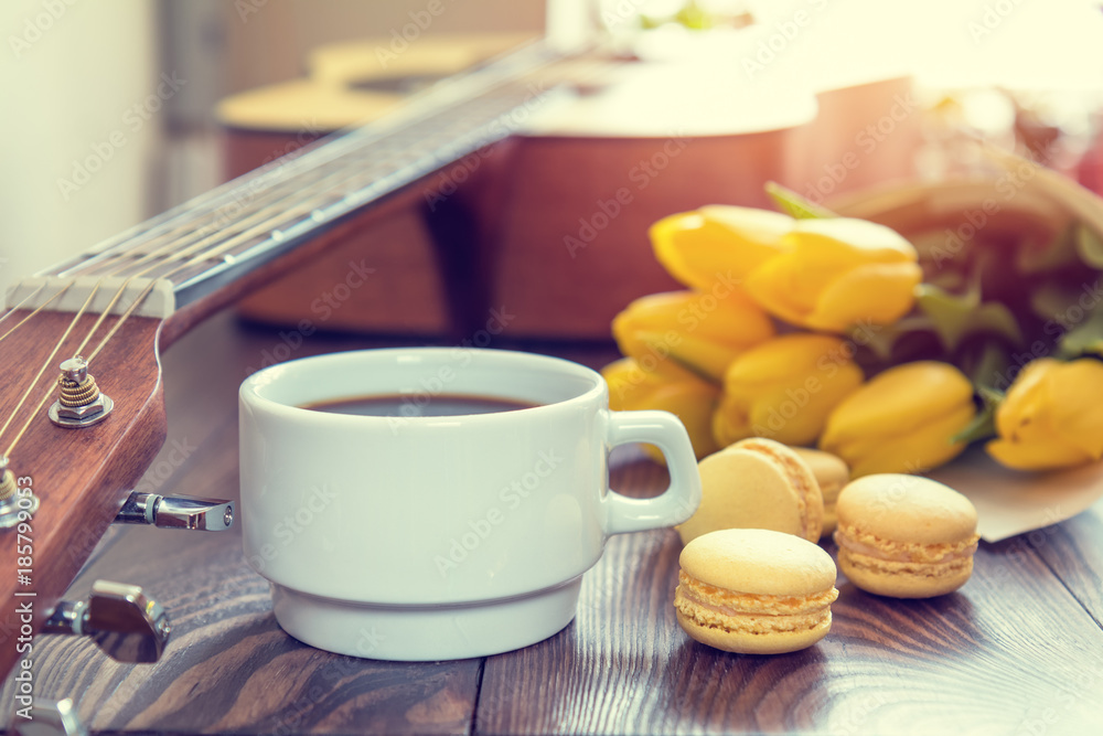 Beautiful spring music background. Cup of coffww, guitar, yellow tulips, musical page on a dark wooden background. Shallow depth of field. Coloring photo with soft focus in instagram style Beautiful spring music background. Cup of coffww, guitar, yellow tulips, musical page on a dark wooden background. Shallow depth of field. Coloring photo with soft focus in instagram style