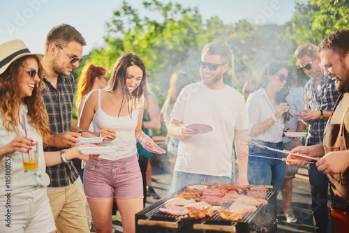 Group of people standing around grill, chatting, drinking and eating Fototapet
