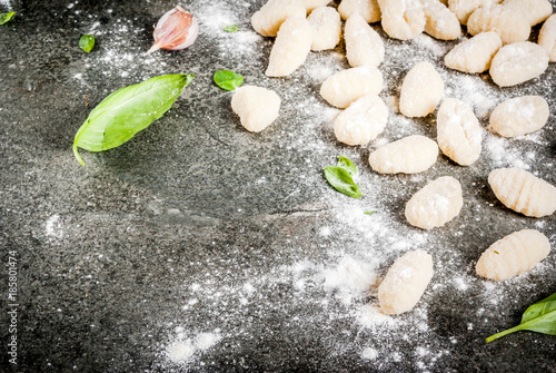 Raw uncooked homemade potato gnocchi with flour, grated parmesan cheese, basil and pesto sauce. On concrete grey background, copy space