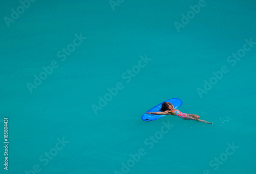 Beautiful fit surfer girl relaxing on blue surfboard in crystal clear turquoise water of the Indian ocean at Padang Padang beach, Bali, Indonesia.