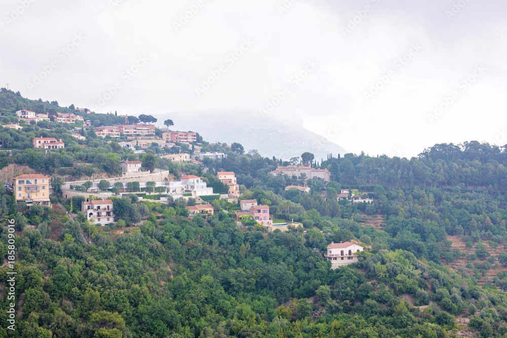 Daylight foggy view to Eze village, trees and mountains from castle