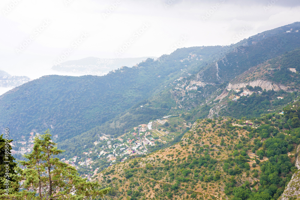 Daylight foggy view to Eze village, Mediterranean sea, trees and mountains