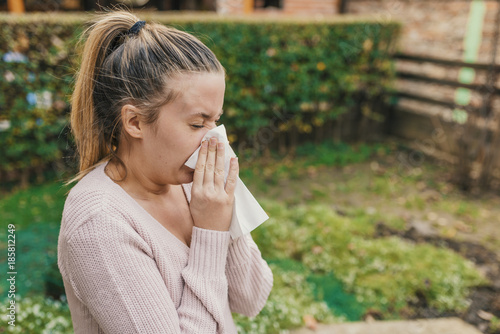 Attractive woman outdoor with tissue having allergy. Woman blowing her nose into tissue