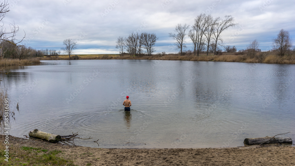 Fototapeta premium Mann mit Weihnachtsmütze geht in einen See zum Baden