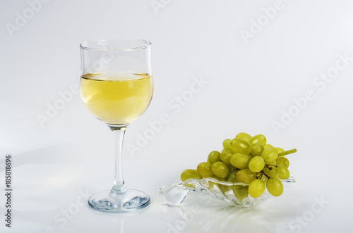 Glass of white wine and a bunch of green grapes on a glass plate