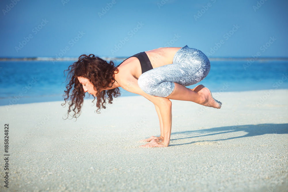 Naklejka premium Summer yoga session on a beautiful golden beach of Maldives yoga tour, Bakasana Crow Crane pose