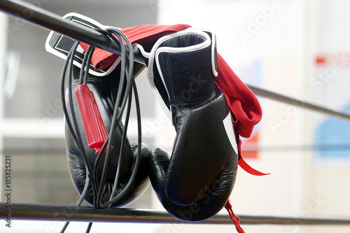 closeup on black boxing gloves  jump rope and red hand wraps hanging on ring ropes