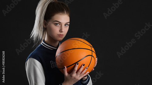 young beautiful girl posing holding basketball ball standing on black background