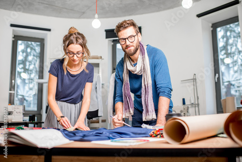 Couple of fashion designers working with fabric at the studio full of tailoring tools and equipment