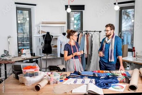 Couple of fashion designers talking at the studio full of tailoring tools and equipment