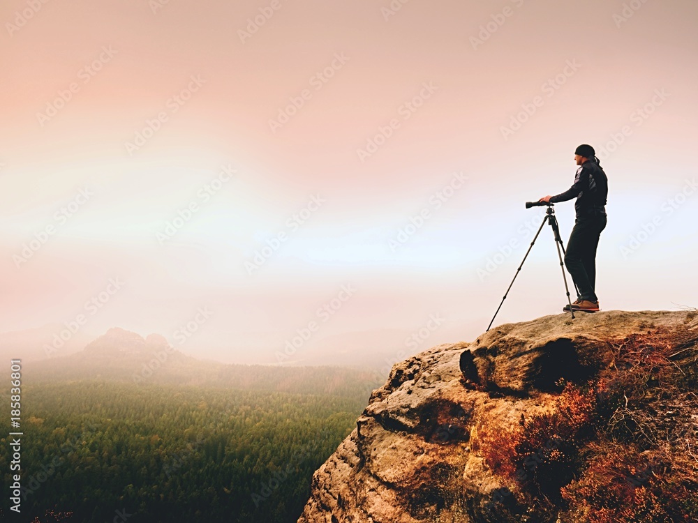 Art photographer on location takes photos with camera on peak of rock. Foggy landscape