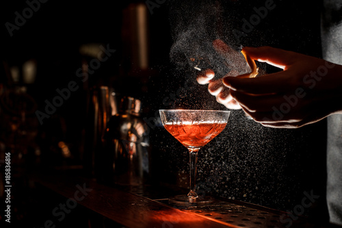 Bartender sprays an orange peel in cocktail glass