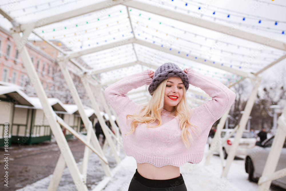Positive young woman with bright makeup wearing knitted hat and sweater, posing at the street in winter Positive young woman with bright makeup wearing knitted hat and sweater, posing at the street in winter