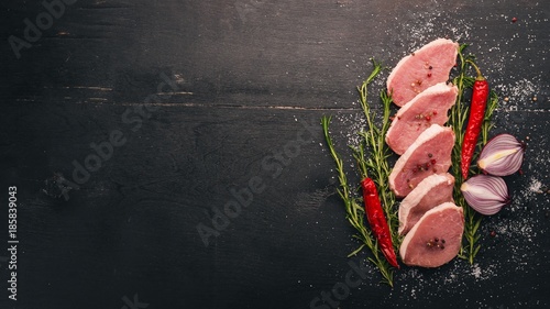 Beef steak with fresh vegetables and rosemary and spices on a black wooden background. Top view. Free space for text.