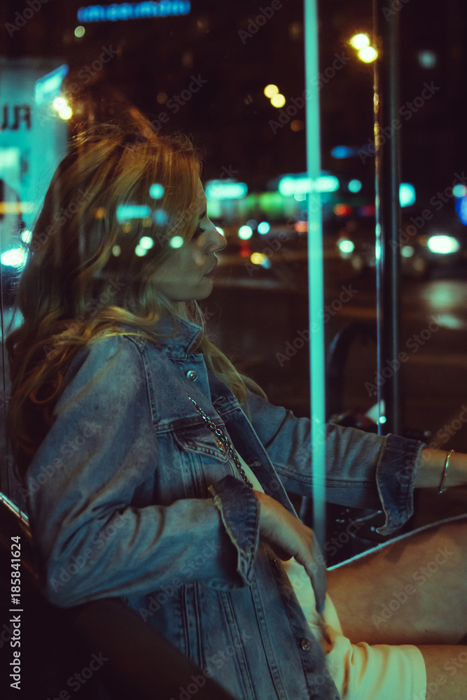 young beautiful blonde girl in black dress strolling by city streets in the evening, sits on a stop in the lights of the night city. young beautiful blonde girl in black dress strolling by city streets in the evening, sits on a stop in the lights of the night city.