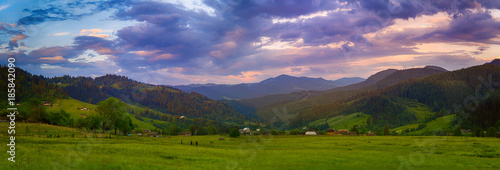 Carpathian mountains summer landscape with cloudy colorful sky and village at sunset, natural travel background