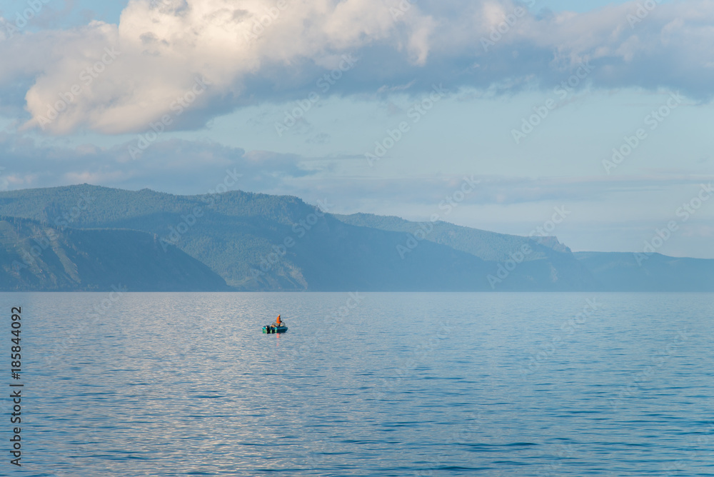 Boat with fisherman on Lake Baikal in calm weather . Blue sky and clouds reflection.