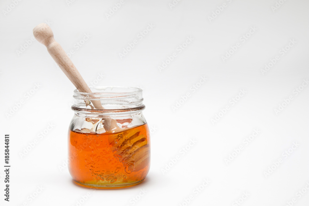 Close up of a decorative honey jar and a honey spoon on a white background with text space Close up of a decorative honey jar and a honey spoon on a white background with text space