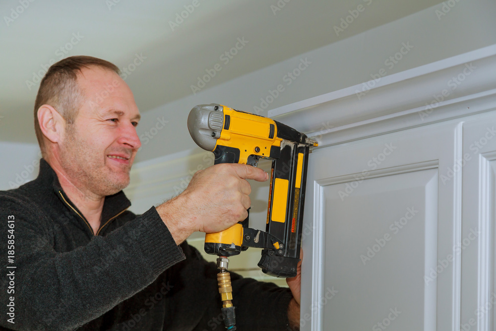 Carpenter using brad nail gun to Crown Moulding on kitchen cabinets framing trim, Carpenter using brad nail gun to Crown Moulding on kitchen cabinets framing trim,
