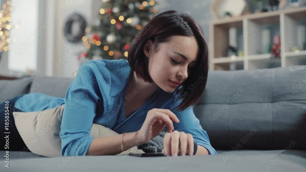 Portrait of beautiful woman uses a smart watches lying on the couch in the background christmas tree closeup watch face elegant finger young slow motion Portrait of beautiful woman uses a smart watches lying on the couch in the background christmas tree closeup watch face elegant finger young slow motion