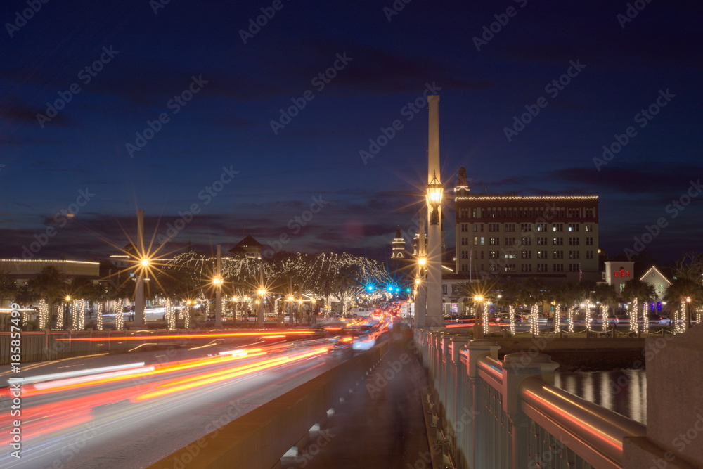 City and bridge decorated with lights at twilight against blue sky showing traffic passing through shot from the bridge looking at the city