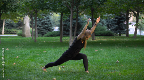 Young girl practicing yoga in the park on the green grass. Early autumn. In the grass are yellow leaves. The girl is young and healthy.