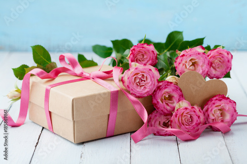 Beautiful greeting card for Birthday, Woman or Mothers Day. Pink rose flowers and gift box with ribbon on turquoise table. Pastel color.