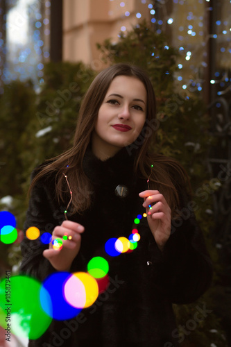 Smiling brunette woman with long hair holding colorful garland at the street