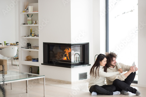 multiethnic couple using tablet computer in front of fireplace