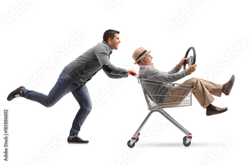 Young man pushing a shopping cart with a mature man riding inside