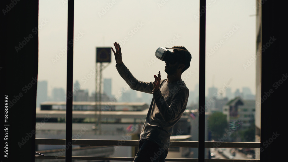Silhouette of young man watching movie in VR headset and have virtual reality experience on hotel room balcony Silhouette of young man watching movie in VR headset and have virtual reality experience on hotel room balcony