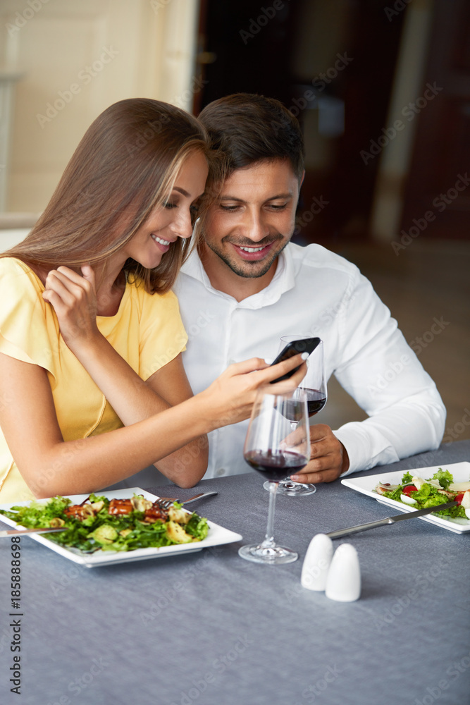 Couple In Love Looking On Phone Having Dinner In Restaurant. Couple In Love Looking On Phone Having Dinner In Restaurant.