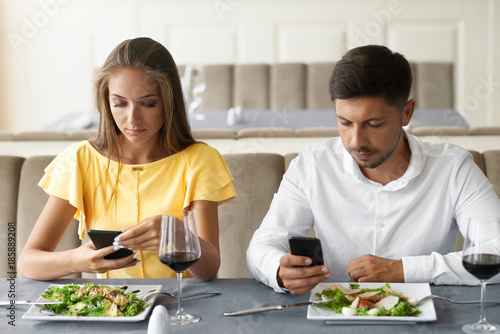 Couple Using Phones On Dinner In Restaurant.