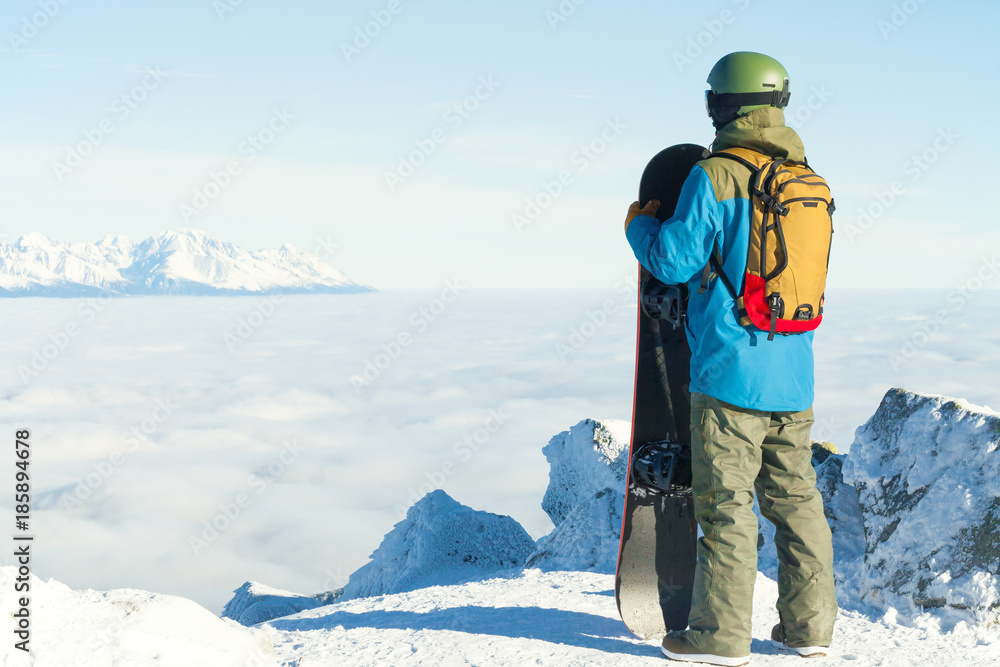 Winter sports concept - young male snowboarder holding board in hands at the very top of a mountain - outdoors shot