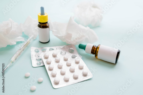 Spray for the nose or a pill to treat colds and gripes. Glass Bottle with medicines and paper handkerchiefs on a green background. Copy space for text photo