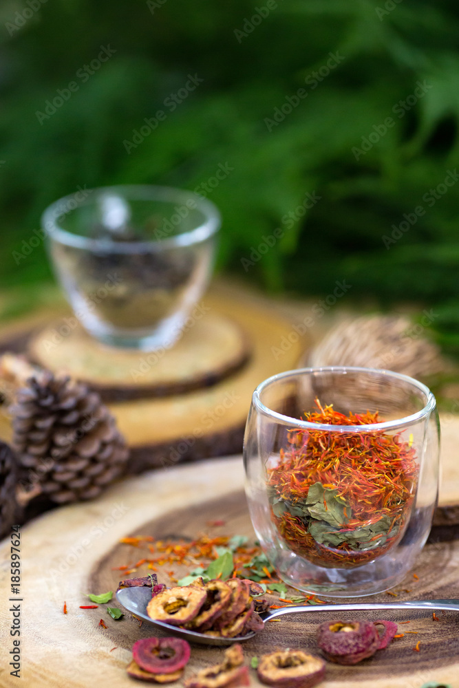 Clear glass cup contains ingredients for making healthy tea is placing on wood slab with pine cone and green leaves for decoration.