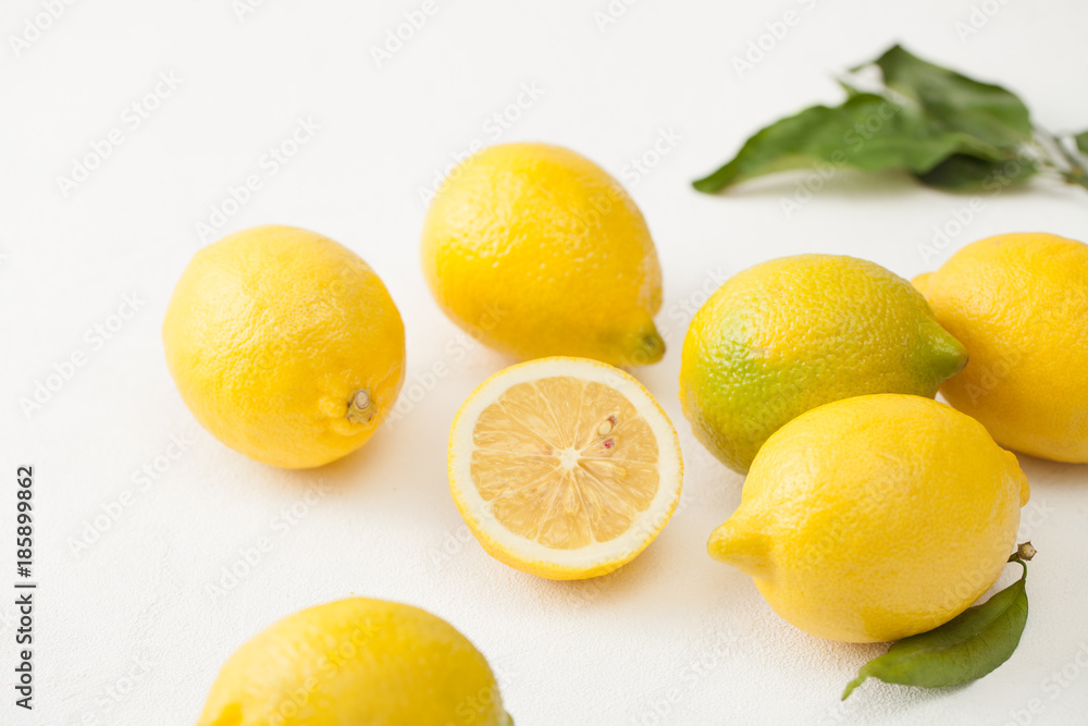 A bunch of lemons with leaves and sliced lemons on a white concrete background.