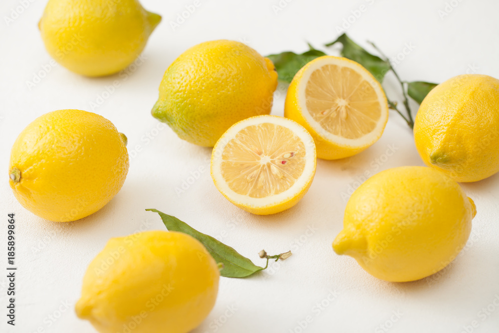 A bunch of lemons with leaves and sliced lemons on a white concrete background. A bunch of lemons with leaves and sliced lemons on a white concrete background.