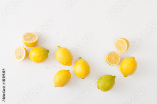 A bunch of lemons and cut lemons on a white concrete background.