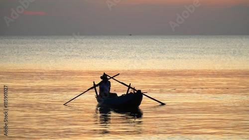 Silhouette at sunset.View from the coast. The boatman in the Vietnamese hat in the small boat..