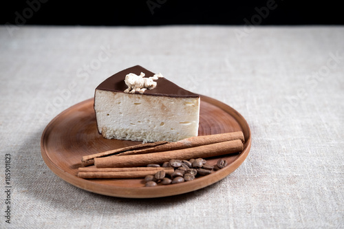 piece of cake with chocolate on a wooden plate with cinnamon sticks and coffee beans on light tablecloth