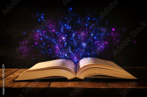 image of open antique book on wooden table with glitter overlay.