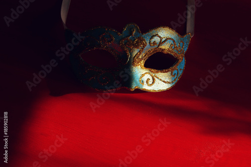Image of elegant blue and gold venetian mask over red background.