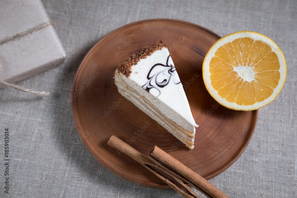 piece of cake with white chocolate and orange and cinnamon sticks lying on a wooden plate next to a holiday gift box and the scattered grains of coffee