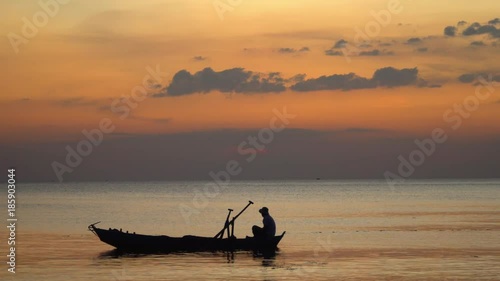 The boatman in the Vietnamese hat in the small boat. The man fishes at sunset. Close up. Silhouette at sunset.View from the coast.